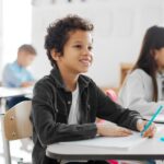 Smiling student writing at his desk representing how to prepare your child for private school and build classroom readiness