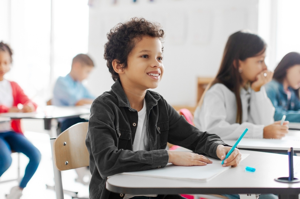 Smiling student writing at his desk representing how to prepare your child for private school and build classroom readiness
