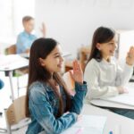 Enthusiastic students raising hands in an engaged classroom environment reflecting the instructional quality that private school accreditation standards require