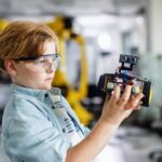 Focused student carefully examining a self-built robot in an engineering lab demonstrating how STEM critical thinking skills develop through hands-on applied learning