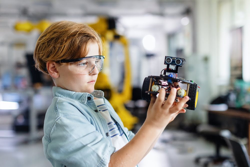 Focused student carefully examining a self-built robot in an engineering lab demonstrating how STEM critical thinking skills develop through hands-on applied learning
