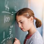Frustrated child leaning against a chalkboard with math equations illustrating the emotional experience of STEM education and math anxiety in elementary school