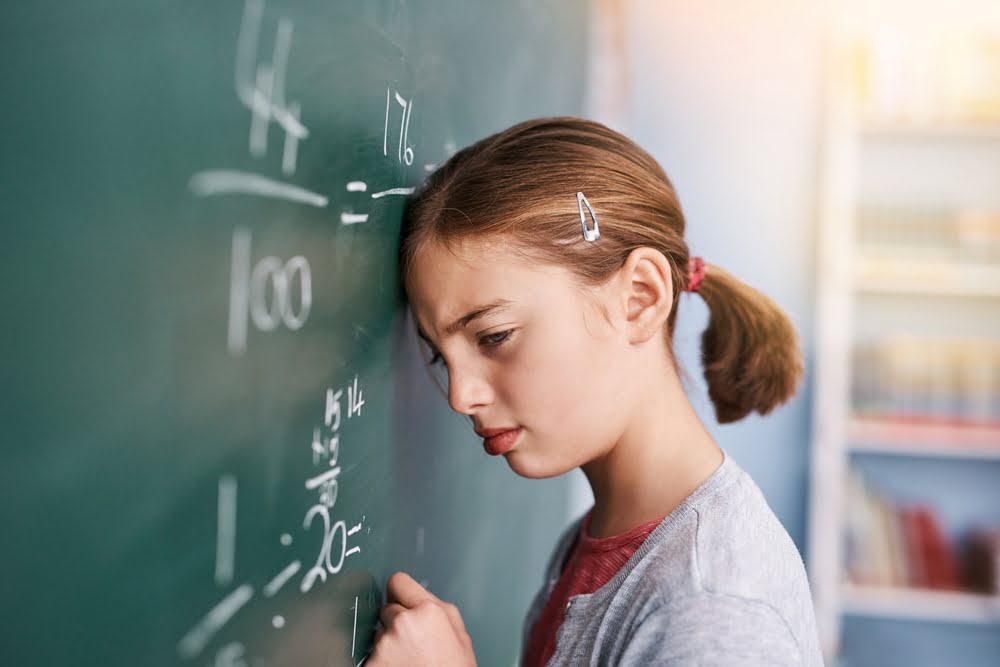 Frustrated child leaning against a chalkboard with math equations illustrating the emotional experience of STEM education and math anxiety in elementary school