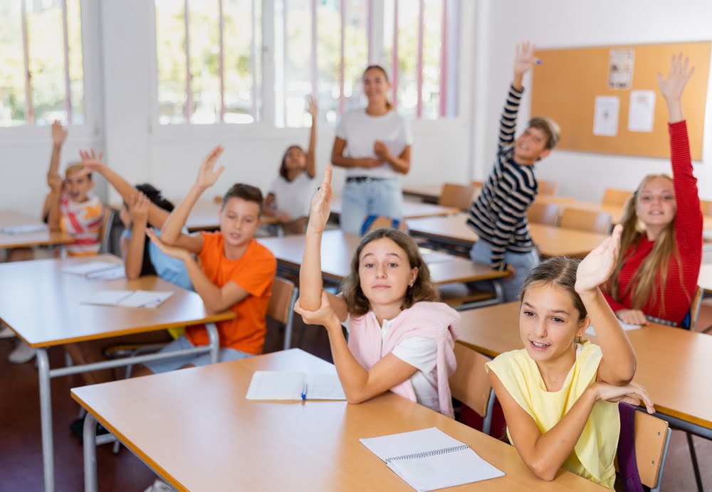 Upper elementary students eagerly raising their hands in class, demonstrating academic engagement, confidence, and the benefits of private school preparation for middle school success.