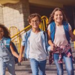 Three happy students with backpacks leaving school together representing the positive adjustment children experience after switching from public to private school