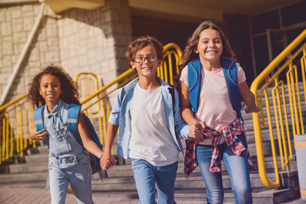 Three happy students with backpacks leaving school together representing the positive adjustment children experience after switching from public to private school