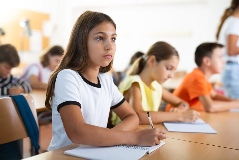 Focused student writing carefully in a notebook at her desk representing the attentive independent work habits that private school reading and writing development builds across the elementary years